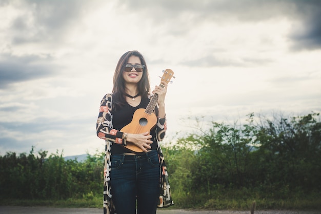 Entspannende Whitbraun-Ukulele der jungen Frau im Park.