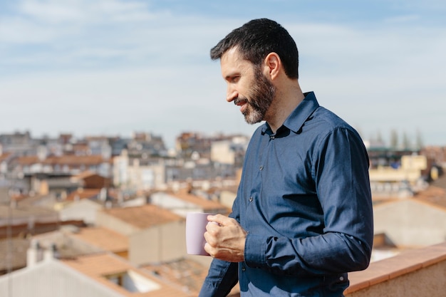 Entspannender Moment eines Mannes mittleren Alters, der auf dem Balkon steht und Kaffee trinkt