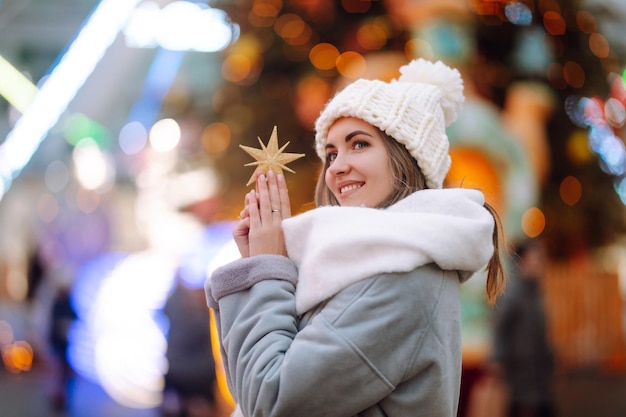 Entspannender trinkender Kaffee der jungen Frau im festlichen Weihnachtsmarkt. Winterferien. Lichter herum.