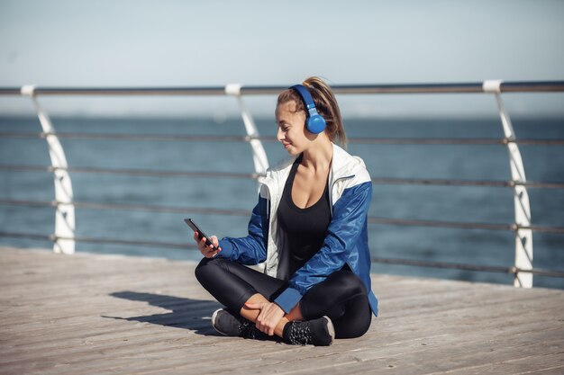 Entspannt fit Frau in Sportbekleidung mit Kopfhörern wählt Musik von einem Smartphone für das Training