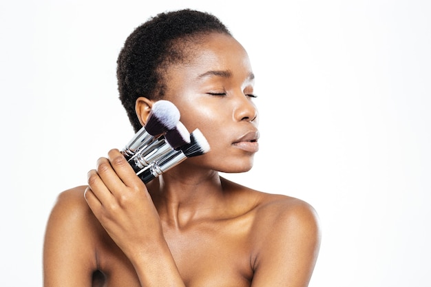 Entspannte afroamerikanische Frau mit geschlossenen Augen, die Make-up-Pinsel auf weißem Hintergrund hält holding