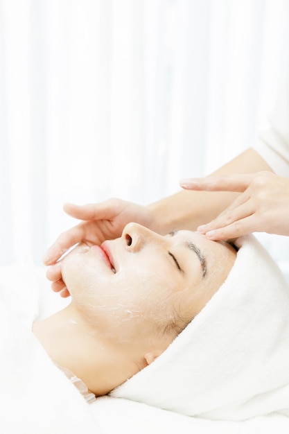 Entspannte asiatische Frau, die eine Gesichtsmassage mit geschlossenen Augen im Schönheitssalon genießt. Gesichtsbehandlung Schönheitsinjektionsverfahren für die Hautpflege