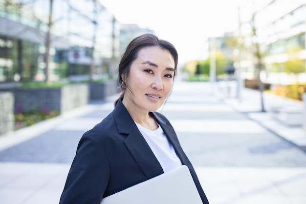 Entspannte asiatische, selbstbewusste Geschäftsfrau im Anzug mit lächelndem Laptop