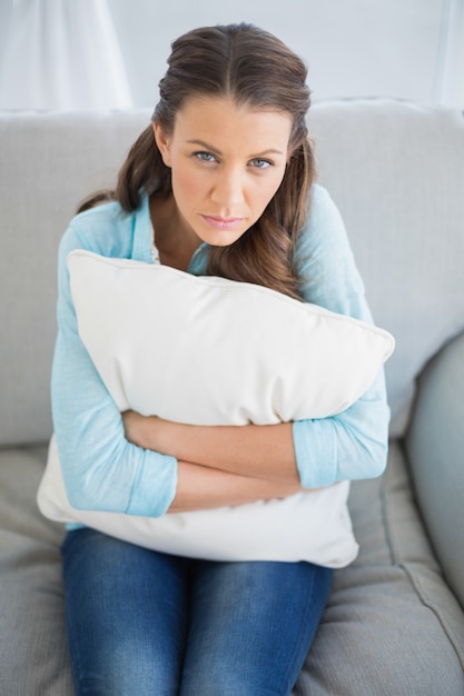 Entspannte Frau, die auf dem Sofa hält Kissen sitzt