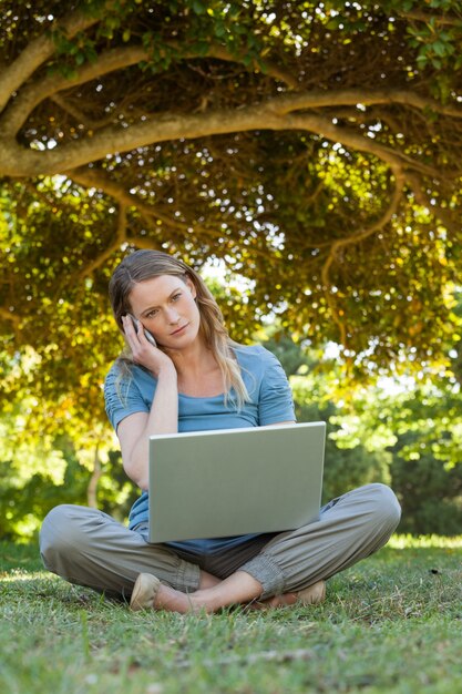 Entspannte Frau, die Laptop und Handy am Park verwendet