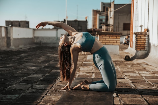 Entspannte Frau, die Yoga-Stretching-Übungen auf einer Dachterrasse praktiziert.