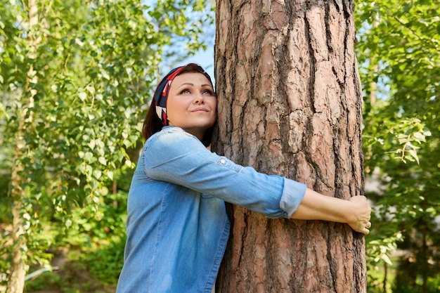 Entspannte Frau mittleren Alters, die die Natur genießt und einen Baum umarmt