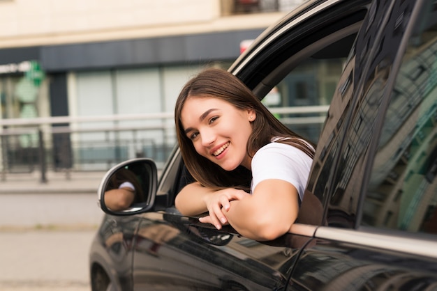 Entspannte glückliche Frau auf Sommer-Roadtrip-Reiseurlaub, der aus Autofenster auf Wand des blauen Himmels lehnt.