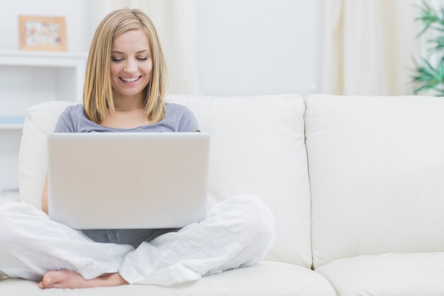 Entspannte glückliche Frau, die Laptop auf Sofa verwendet