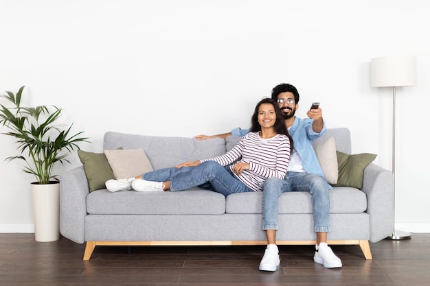 Entspannte indische Ehepartner sitzen auf dem Sofa und schauen sich Filme im Fernsehen an