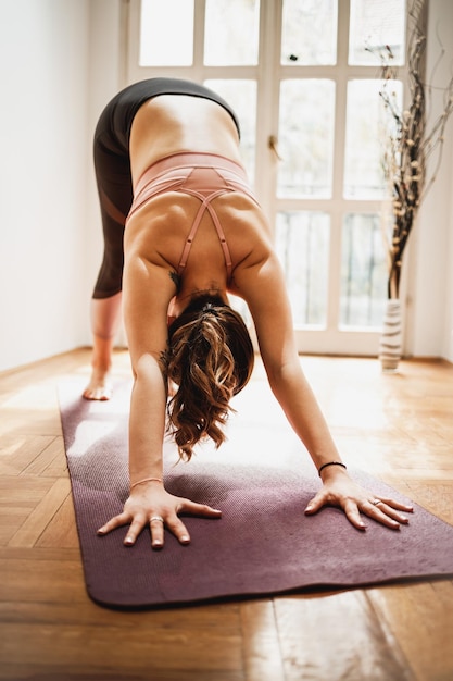 Entspannte junge Frau, die zu Hause Yoga in Ado Muka Svanasana-Pose praktiziert.