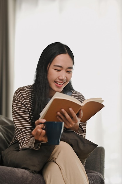 Entspannte junge Frau in lässiger Kleidung, die ein Buch liest und ihre Freizeit am Wochenende zu Hause verbringt