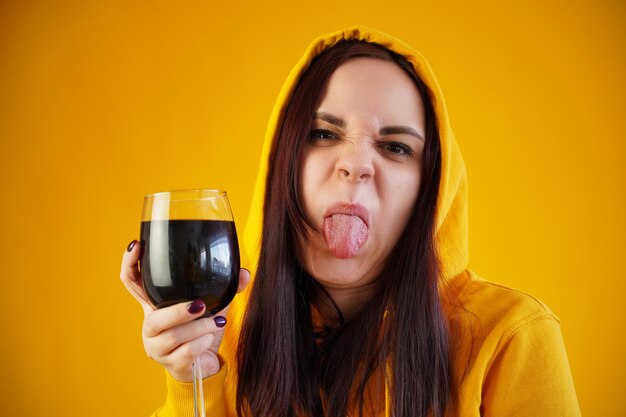 Entspannte junge Frau posiert mit einem Glas Rotwein auf gelbem Hintergrund Erwachsene glückliche Brünette, die sich an ihrem Wochenende mit Alkohol ausruht