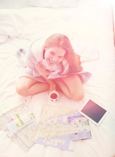 Entspannte junge Frau sitzt auf dem Bett mit einer Tasse Kaffee und digitalem Tablet