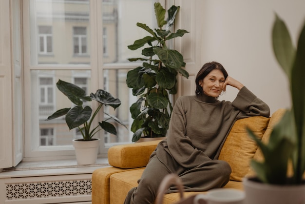 Entspannte kaukasische erwachsene Hausfrau, die auf einem bequemen Sofa im Wohnzimmer sitzt und Sonntagmorgen plant Konzept der Ruhe und Erholung