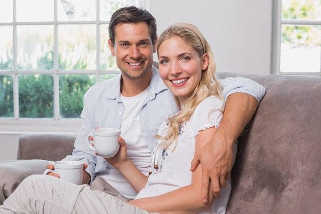 Entspannte liebevolle Paare mit den Kaffeetassen, die auf Sofa sitzen