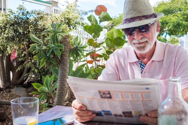 Entspannte Momente für einen älteren Rentner, der im Garten sitzt und eine Zeitung liest. Tropische Pflanzen und sonniger Tag
