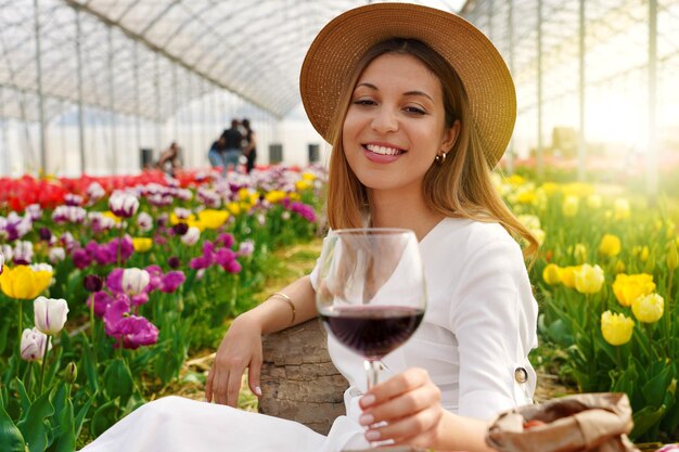 Entspannte schöne Frau, die im Frühling ein Glas Rotwein zwischen Tulpen genießt