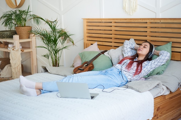 Entspannte schöne Frau mit geschlossenen Augen hört Musik mit Kopfhörern, die auf dem Bett liegen.