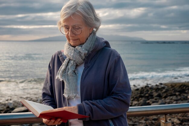 Entspannte Seniorin im Ruhestand auf See, die ein Buch bei Sonnenuntergang atlantik auf den Kanarischen Inseln von Teneriffa liest Reise- und Freiheitskonzept