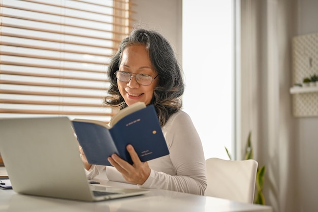 Entspannte und glückliche asiatische Frau aus den 60er Jahren, die an ihrem Arbeitsplatz ein Buch liest