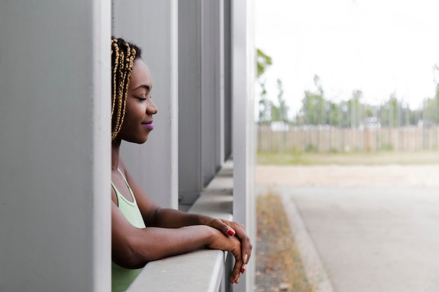 Entspannte und ruhige junge Afroamerikanerin mit langen blonden Zöpfen lehnt sich mit geschlossenen Augen auf den Balkon. Platz kopieren.