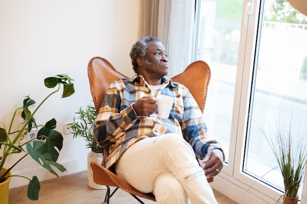 Entspannter älterer Mann, der am Fenster einen Kaffee trinkt und nach draußen schaut. Konzept Ruhe, Trennung, Ruhestandsleben