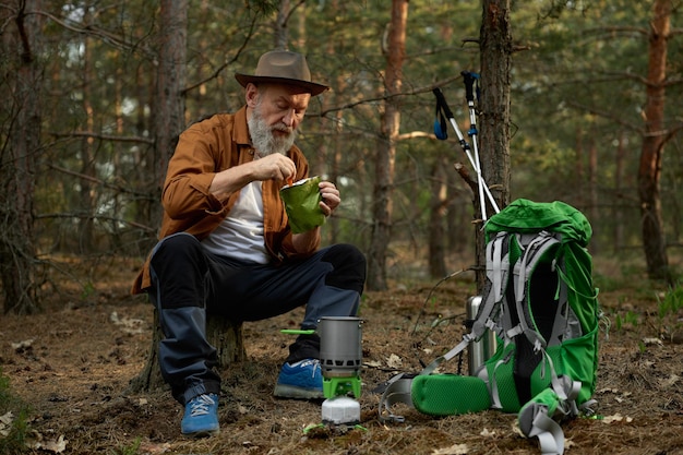 Foto entspannter älterer wanderer, der nach einem touristischen ausflug im wald essen isst und eine pause macht. outdoor-abenteuer im ruhestand