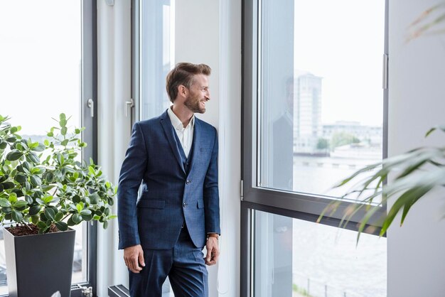 Entspannter Geschäftsmann, der in seinem Büro steht und aus dem Fenster schaut