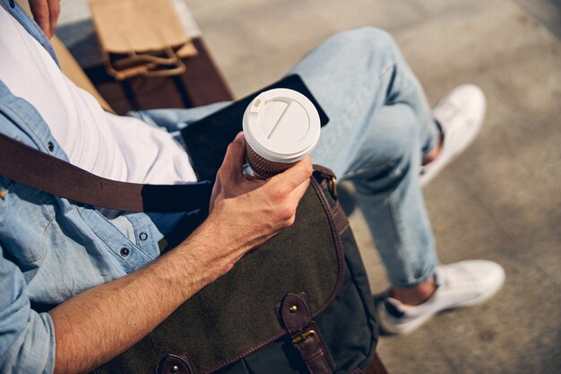 Entspannter junger Mann, der sich nach der Arbeit ausruht und Nachrichten online liest, leckeren Kaffee trinken wird