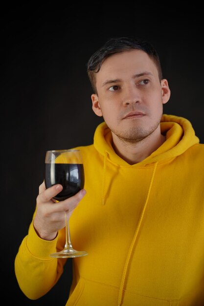 Entspannter junger Mann posiert mit einem Glas Rotwein auf schwarzem Hintergrund Erwachsener glücklicher Kerl, der sich an seinem Wochenende mit Alkohol ausruht