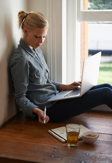 Entspannter Nachmittag Eine junge Frau, die auf einem Boden sitzt und auf ihrem Laptop recherchiert