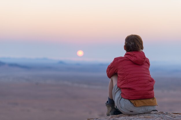 Entspannter Tourist, der auf Felsen sitzt und den Sonnenuntergang betrachtet