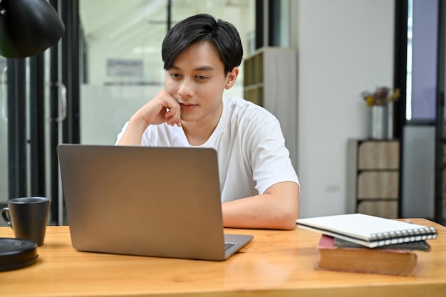 Entspannter und ungezwungener asiatischer männlicher Student oder männlicher Büroangestellter mit Laptop