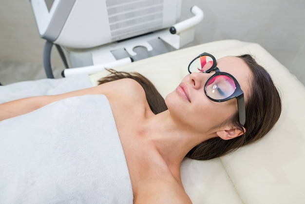 Entspanntes junges Mädchen liegt mit Gelassenheit auf dem Massagetisch Sie trägt eine Schutzbrille für das Laserverfahren