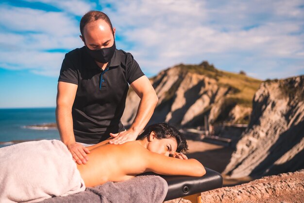 Entspanntes Mädchen bei der Massage an der Küste nahe der Meeresmasseurin mit Gesichtsmaske