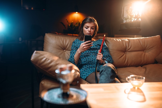 Entspannung der jungen Frau, rauchende Wasserpfeife an der Bar. Mädchen raucht Shisha im Nachtclub