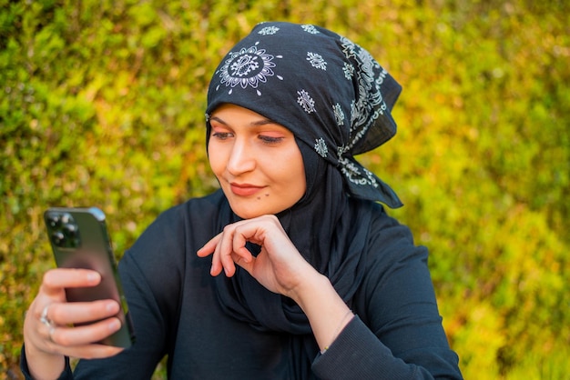 Entspannung mit einem Mobiltelefon Pausenzeit Junge muslimische Frau benutzt Mobiltelefon und sitzt auf dem GrasSu
