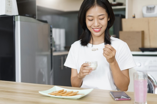 Entspannungskonzept zu Hause Junge Frau, die Joghurt isst und in der Freizeit zu Hause auf dem Smartphone schaut