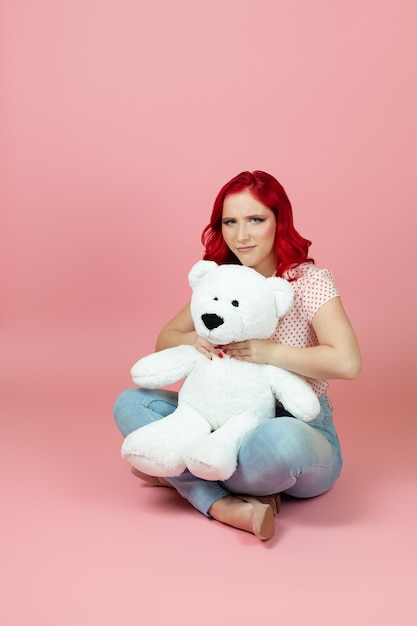 Enttäuschte Frau erwürgt einen großen weißen Teddybären am Hals, der auf dem Boden sitzt