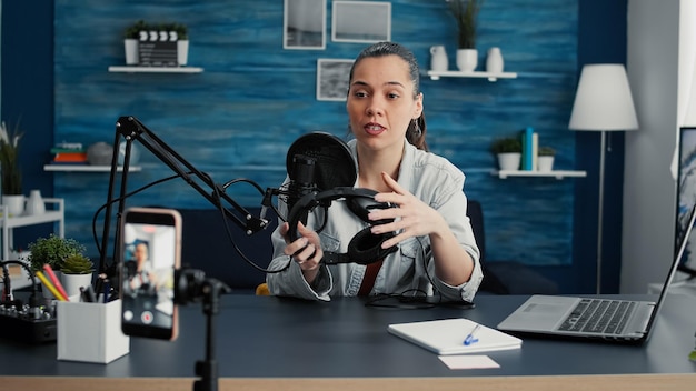 Entusiasta de tecnologia popular revisando fones de ouvido modernos enquanto grava vídeo de recomendação no estúdio da sala de estar em casa. Famoso influenciador de mídia social fazendo clipe de promoção de produto para fones de ouvido.