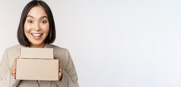 Entusiasta empresaria asiática dando cajas de pedidos de clientes de pie contra el fondo blanco.