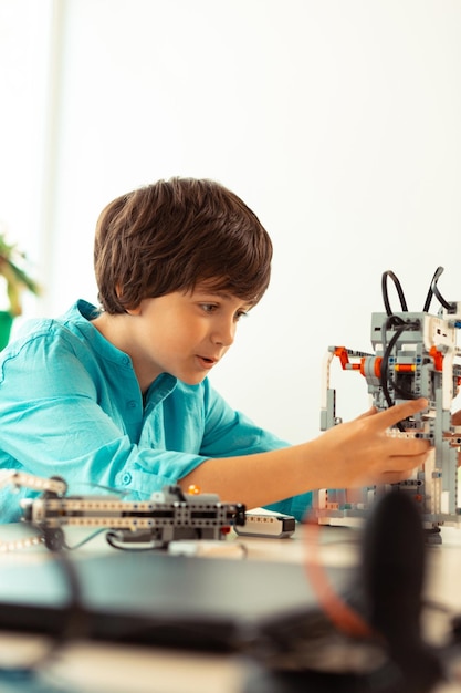 Foto entusiasta estudiante de primaria construyendo diferentes figuras con juego de construcción durante su lección de ciencias