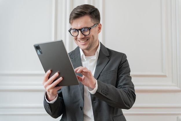 Un entusiasta hombre de negocios vestido con un elegante traje gris navega por una tableta con una expresión de satisfacción