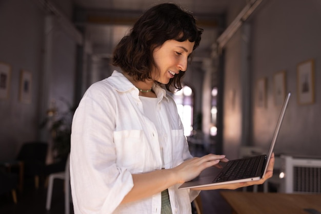 Entusiasta joven morena caucásica con camisa blanca usa un cuaderno en el lugar de trabajo en el interior Concepto de tecnología todos los días