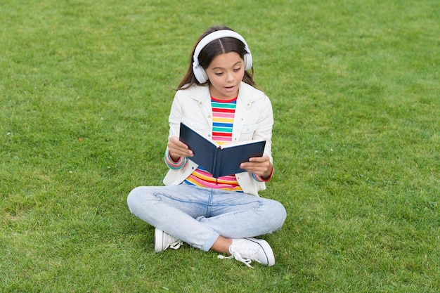 Entwicklung der Fantasie süßes Mädchen las Buch glückliches Vorschulmädchen mit Buch im Schulhof zurück zur Schule fleißiges Kind im Kopfhörer Konzept der Bildung und des Lesens ein Schriftsteller sein