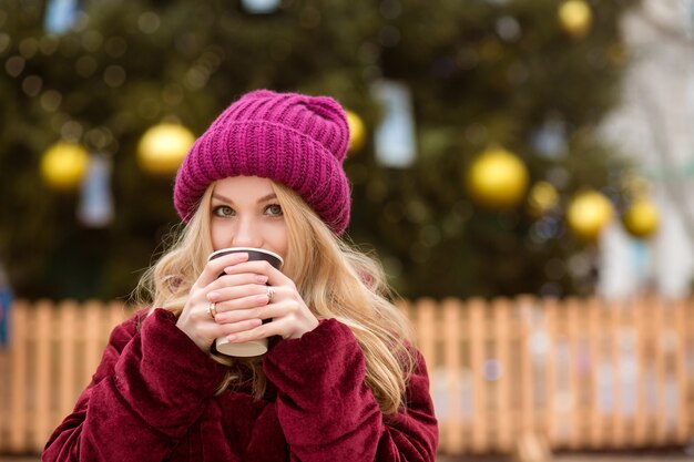 Entzückende blonde Frau, die Kaffee in der Nähe des Christmas-Baums auf dem zentralen Platz in Kiew trinkt