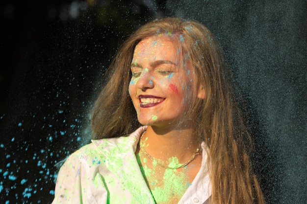 Entzückende blonde Frau im weißen Hemd, die das Holi-Festival im Park feiert