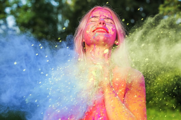 Entzückende blonde Frau mit explodierender bunter Farbe, die das Holi-Festival feiert