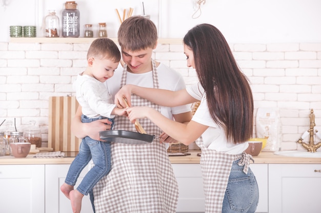 Entzückende Familie, die zusammen kocht. Junge Familie in der Küche beim Frühstück oder Abendessen. Mama, Papa und ihr kleines Kind bereiten Essen zu.